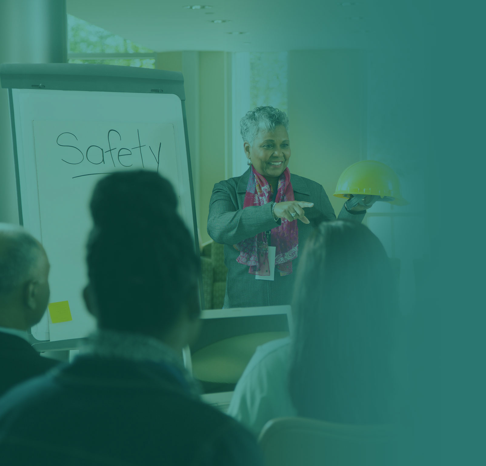 Female instructor leading a Full Spectrum Safety Consulting safety training presentation, holding a hard hat and engaging employees.